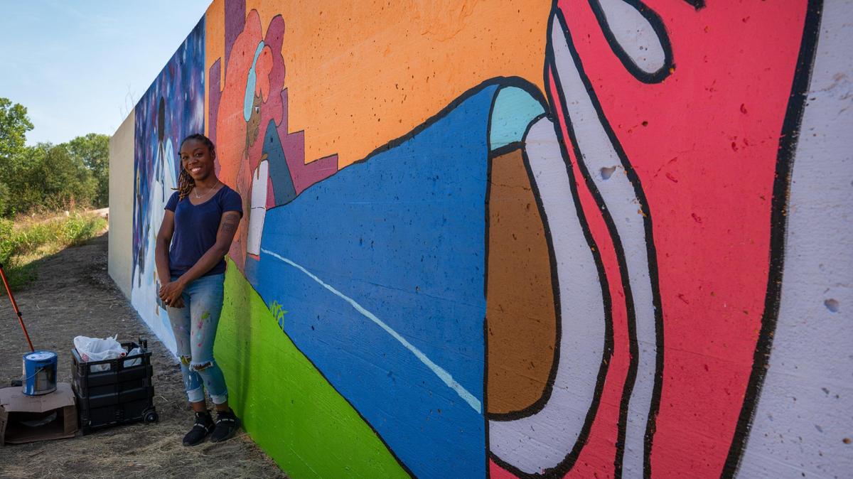 Jasmine Ali stands for a portrait near her mural “Growth” on Friday, Sept. 15, 2023, at the Riverfront Heritage Trail in Kansas City. Ali has worked as a professional artist for seven years and is a part of the first group of artists painting murals on the concrete wall.