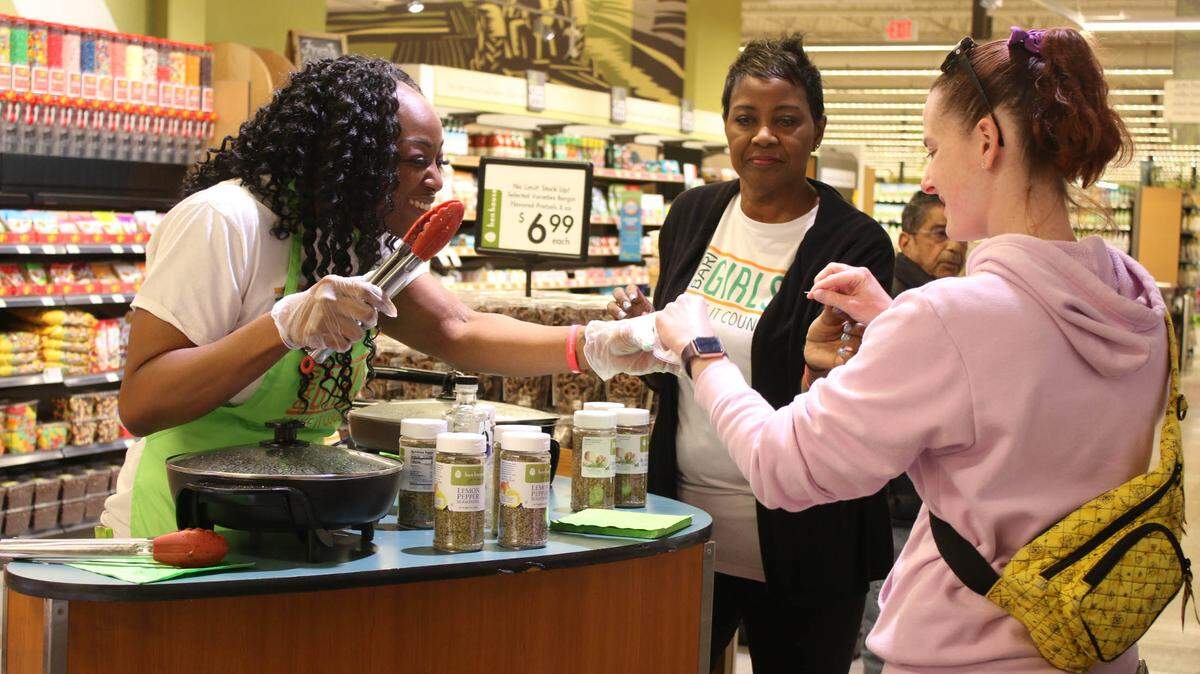 Kiley Williams-Bowls offers shopper Lilly Heller a food sample at Hen House Market in Leawood as Linda Donaldson watches. The BariGirls have a partnership with the grocery store that involves both making cooking videos and doing in-store sampling events.