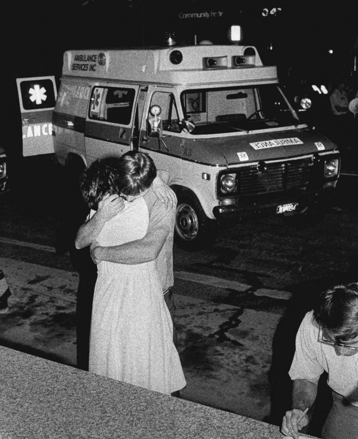A man and a woman embrace in a hug outside of the Hyatt while rescue efforts go on inside.