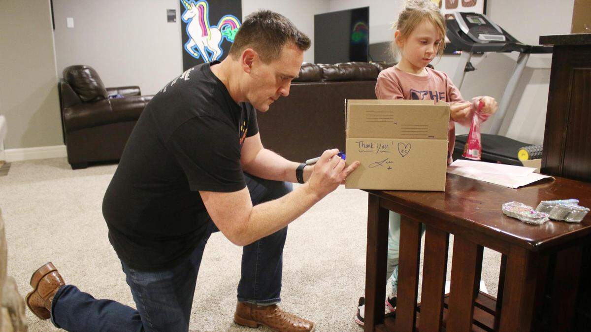 Lee Urban and Charlotte Urban, 7, work together to package a shipment of some bags of Troll Turds candy in the basement of their Shawnee home. Each box comes with both their signatures and artwork from Charlotte.