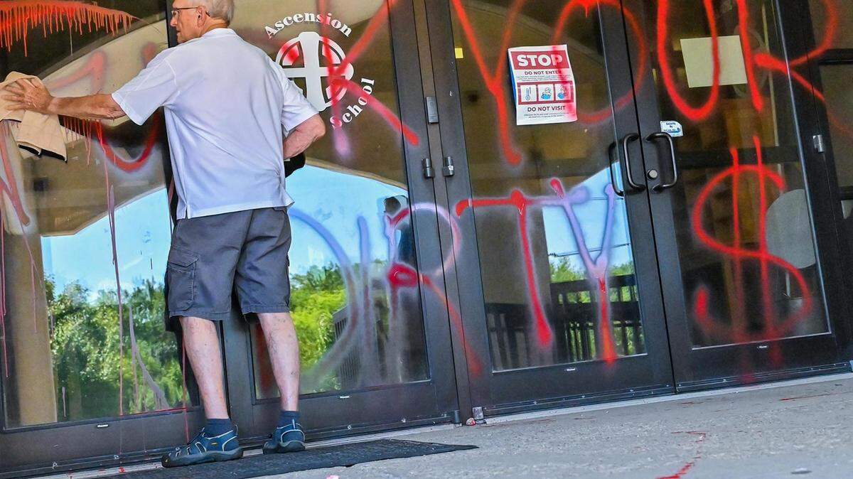 A man cleaned red paint sprayed across the entry of Ascension Catholic School in Overland Park, which is adjacent to Church of the Ascension, on Sunday.