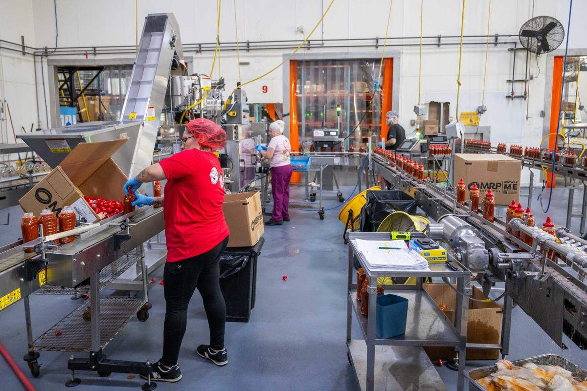 Employees of Spicin Foods put lids on bottles of sriracha hot sauce on the production floor at the Spicin Foods warehouse on Southwest Boulevard, on October 2, 2025,  in Kansas City. Spicin Foods not only makes their own sauces but also serves as a maker and bottler of other well-known sauces on the market.