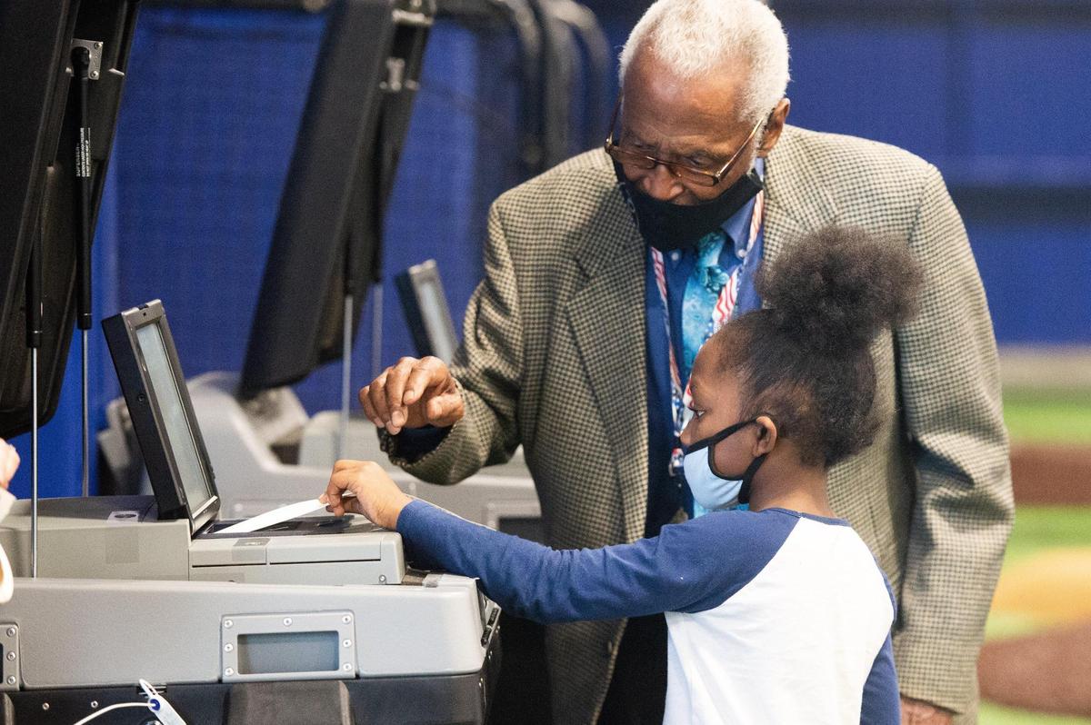 Aarriana Wilson, 7, cast a paper ballot in the voting machine for her mother, Keya Wilson (not pictured), with the help of an election volunteer at the Kansas City Urban Youth Academy Tuesday afternoon. Over 500 people had voted by noon there.