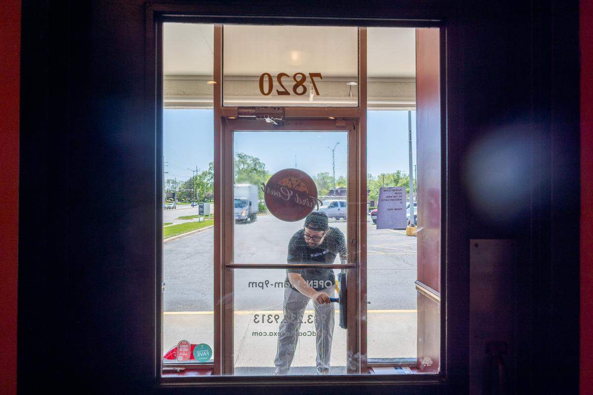 Davis Roethler cleans the front windows of Third Coast Pizza in Lenexa, on Monday, April 20, 2026. Roethler, whose company is named Window Wolf, uses social media to shine a light on small businesses and also cleans their windows for free.
