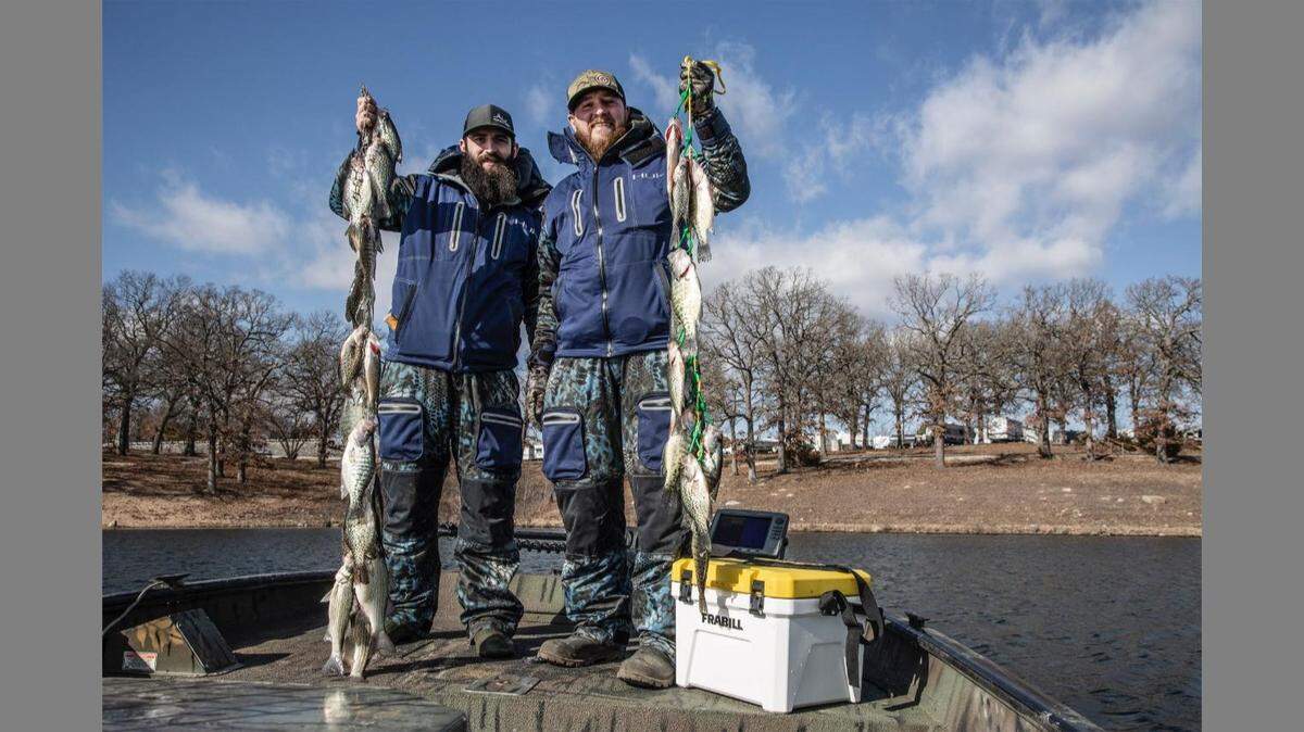Josh Matthews (left) and Devin Greenwood hoisting their stringers of crappie caught on Pomme de Terre with guide Kris Nelson of Tandem Fly Outfitters. Although they battled cold and windy conditions, Nelson was able to find the fish transitioning from brush piles to deeper water for the winter.