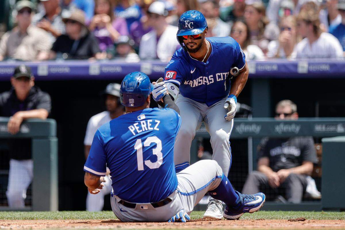 Royals captain Salvador Perez gets a hand up from left fielder MJ Melendez after sliding to score during KC’s big second inning Sunday at Coors Field.