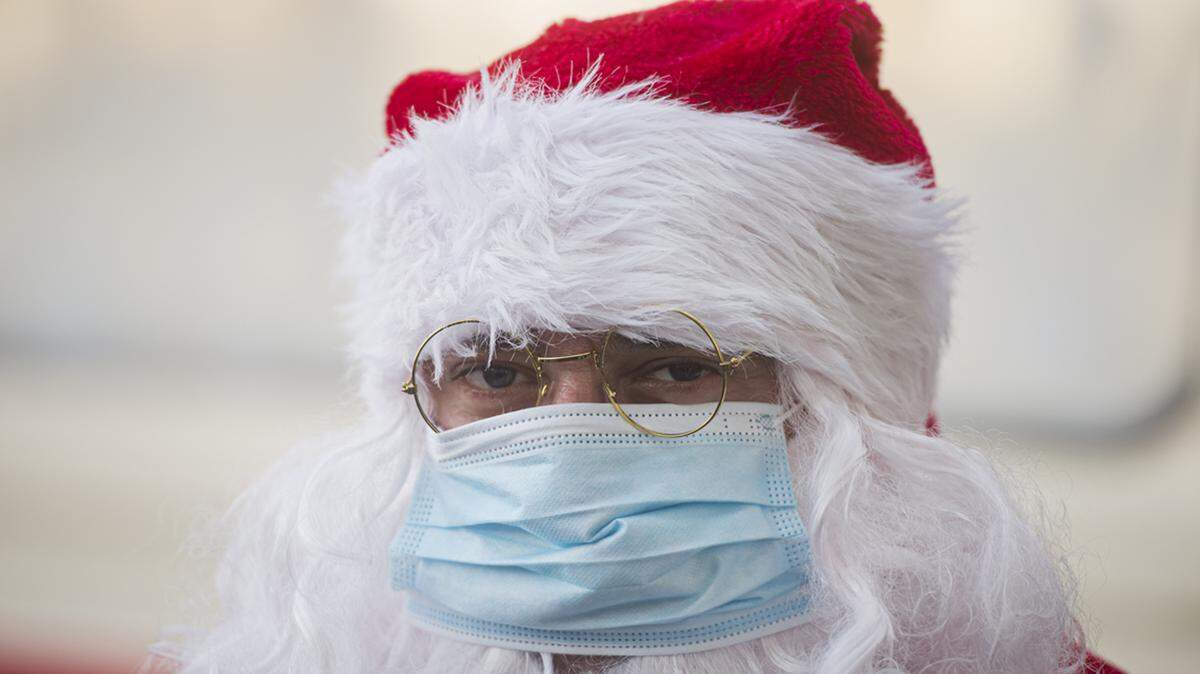 A person wearing a Santa Claus outfit and a mask for protection against COVID-19 infection stands during a Christmas event.