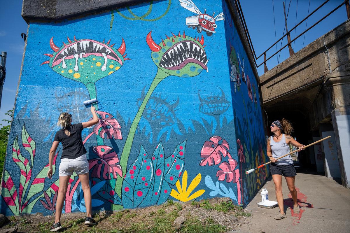 Sister Michelle Renn of Kansas City, left, a graphic designer, and muralist Merry Burleson, of Harrison, Arkansas, paint their mural on the southeast corner of the bridge. The mural called “Venus Fly Truck” was designed by Renn.