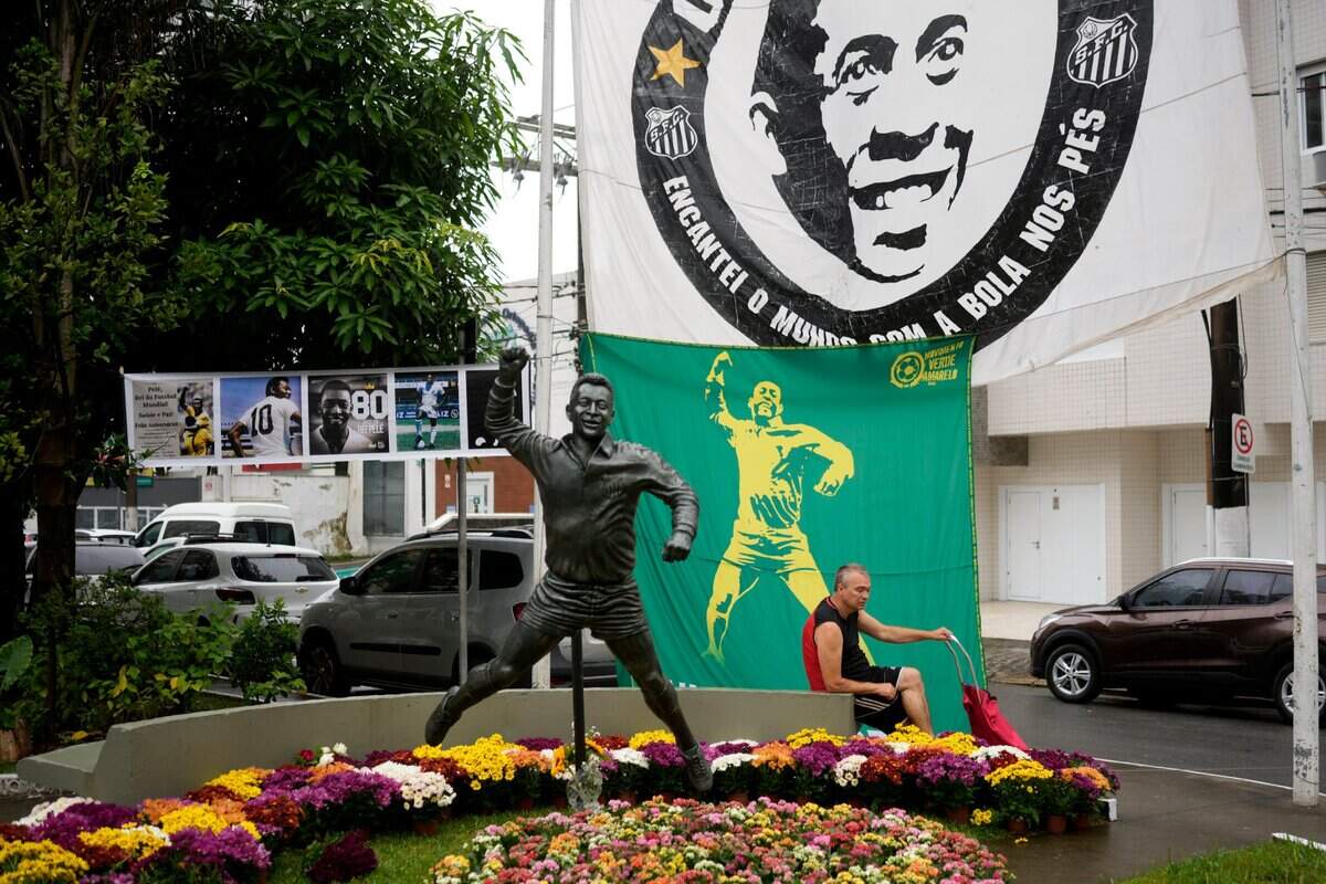 A man sits next to a statue of the Brazilian soccer star Pele in Santos, Brazil on Friday, the day after the soccer legend’s death in São Paulo at the age of 82.