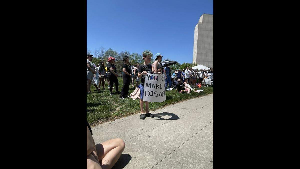 Woods Haren, 8, lifted a sign they had drawn in the crowd of people gathered Saturday in Ilus Park to protest restrictions on gender-affirming care.