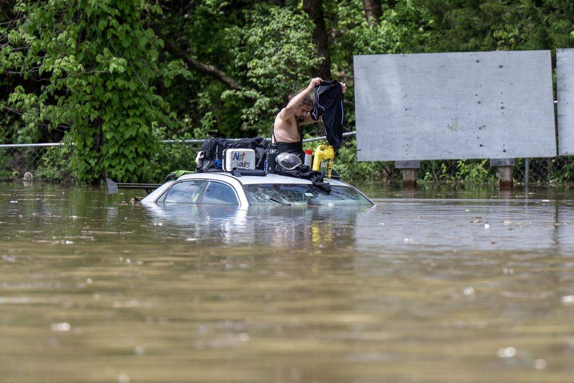 A person sits on top of a vehicle surrounded by flooding waters near the Fisca gas station at the corner of Old 23 Street and Television Place on Monday, April 27, 2026, in Kansas City.