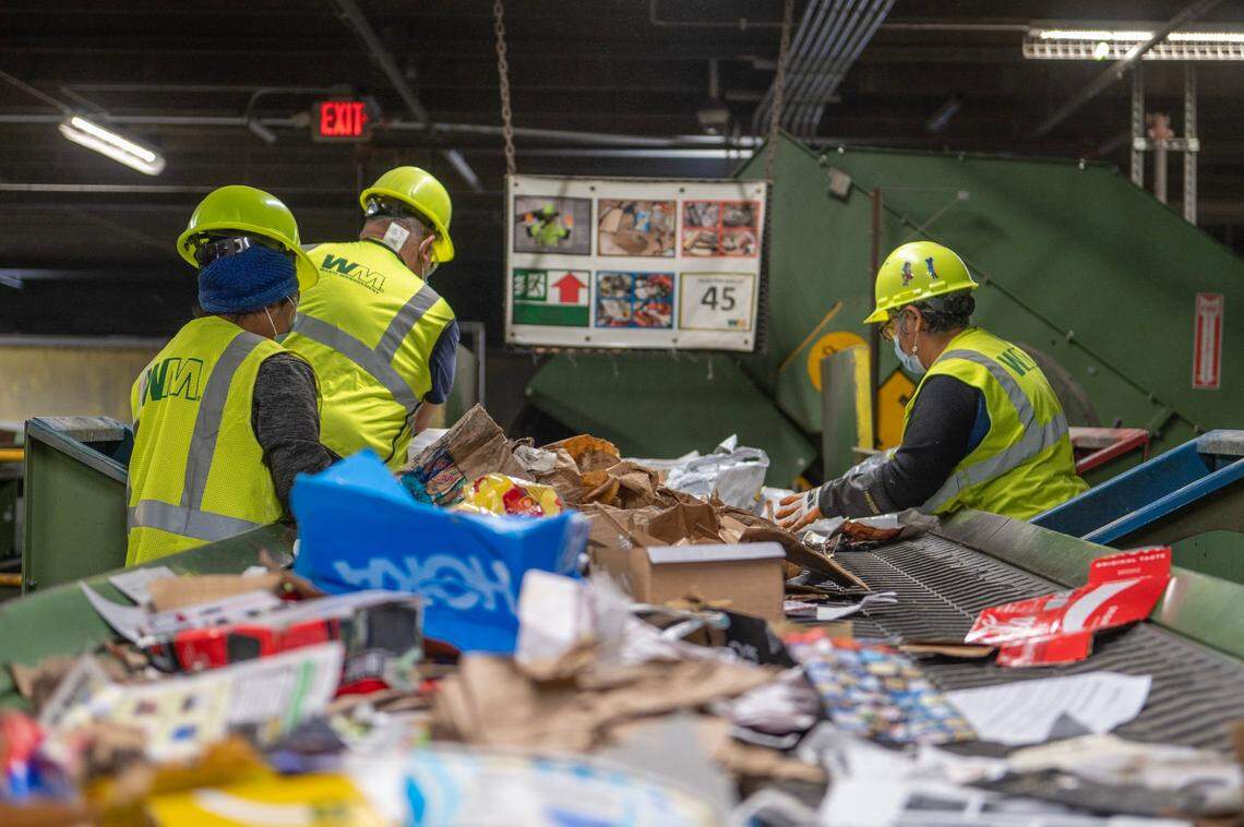 Waste Management employees manually separate recycling materials from a conveyer belt at the Waste Management recycling facility on Thursday, March 16, 2023, in Kansas City, Kan.