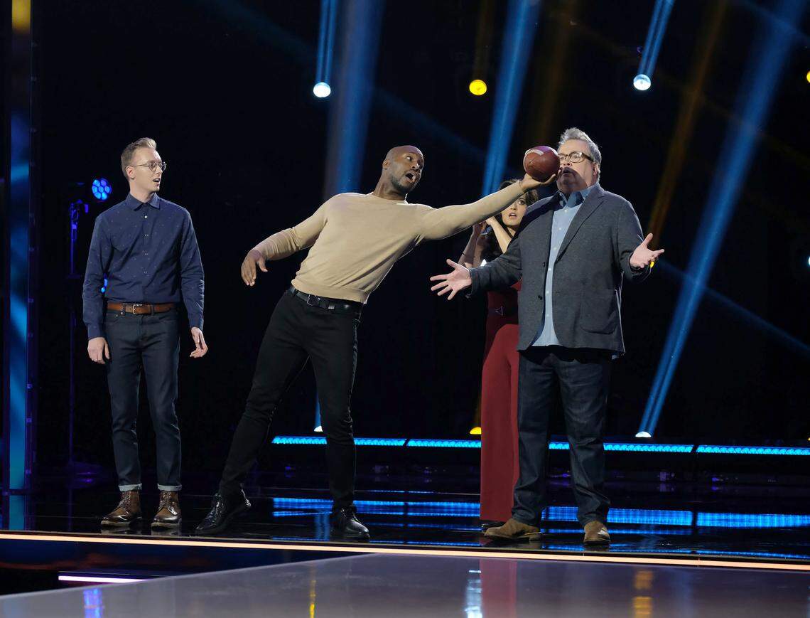 “Domino Masters” judge Vernon Davis shows he hasn’t forgotten his skills as an NFL tight end as a football heads toward host Eric Stonestreet. Looking on are judges Steve Price and Danica McKellar.