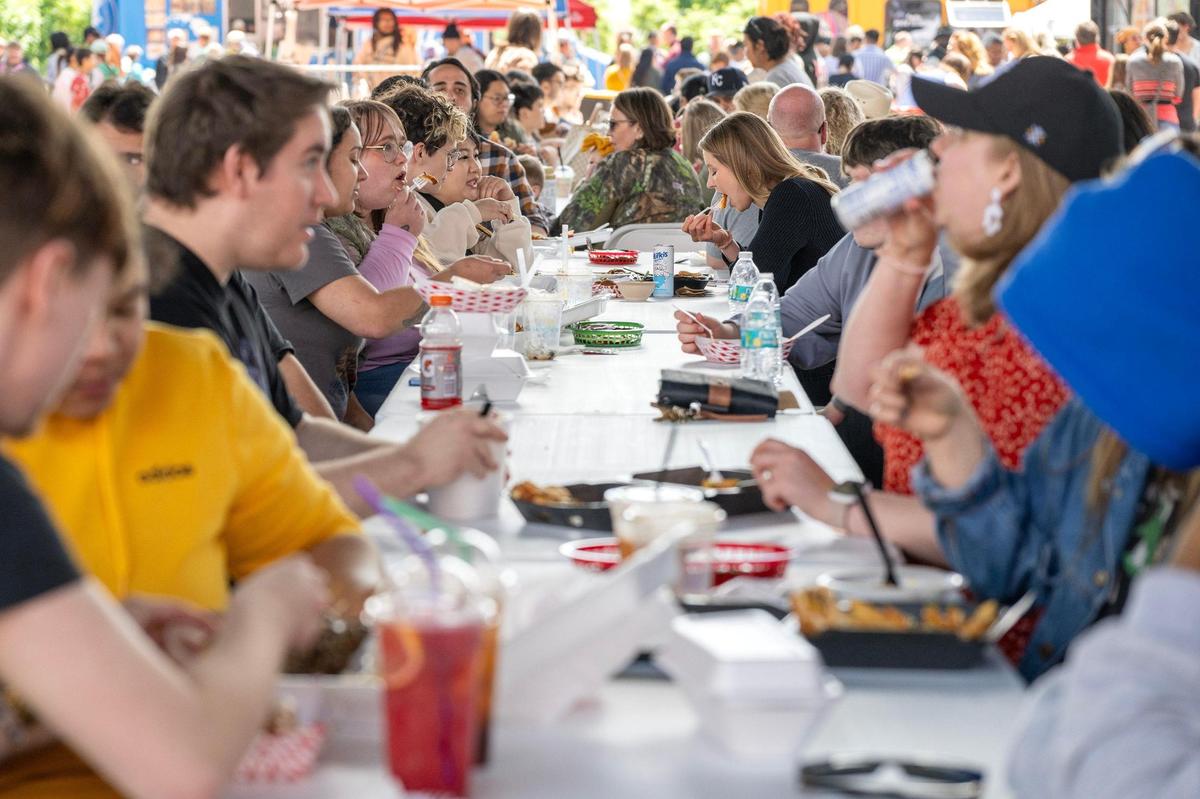 Visitors eat at a continuous row of tables set up for communal dining during the 4th Annual Taste of AAPI festival on Saturday, May 3, 2025, in the West Bottoms district of Kansas City. The event celebrates Asian American and Pacific Islander Heritage Month with food vendors, cultural performances and community activities.