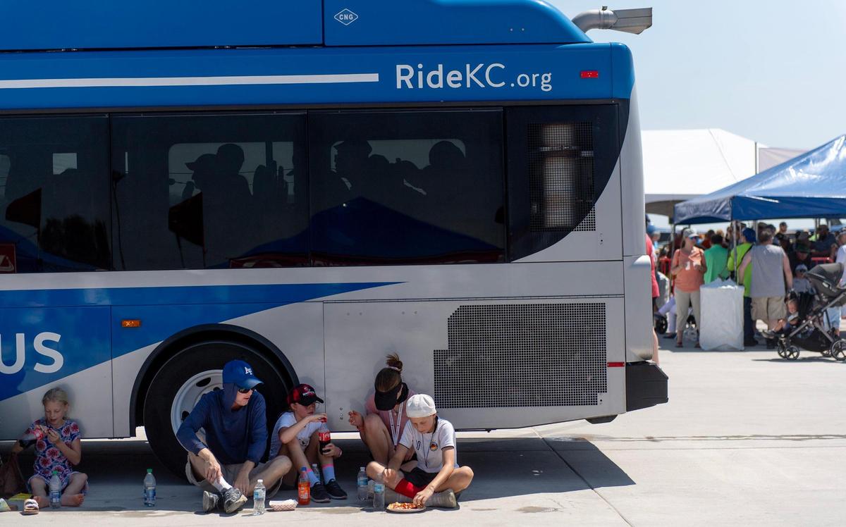 People eat in the shade cast by a RideKC bus during the Garmin KC Air Show on Saturday, Aug. 19, 2023, in New Century.