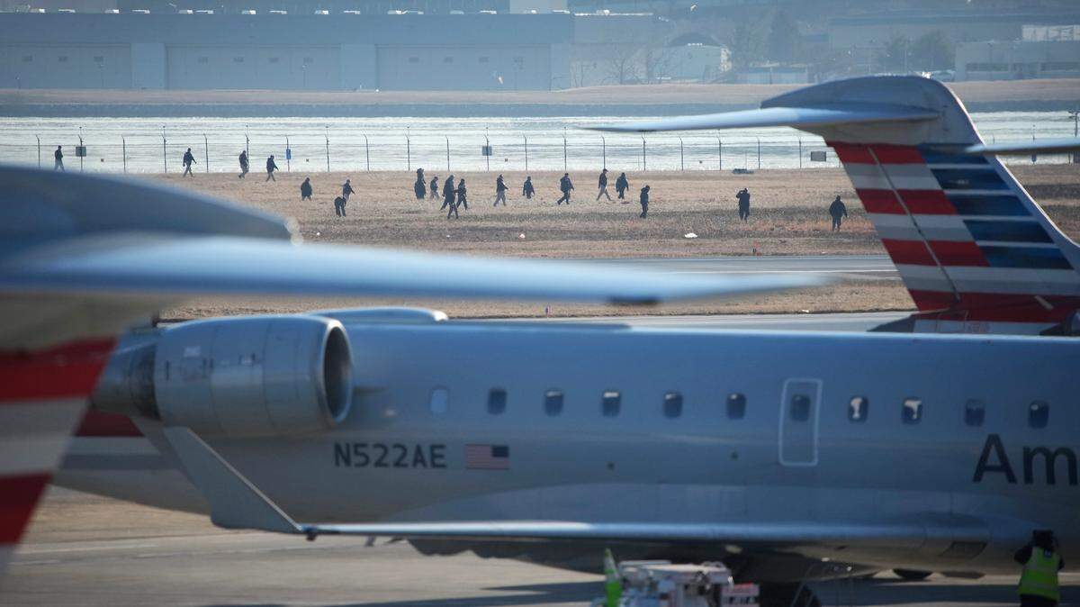 Investigators walk the grounds of the Reagan National Airport Thursday after Wednesday night’s collision of an American Airlines airliner and a military Black Hawk helicopter over the Potomac River as the plane approached the airport for a landing.