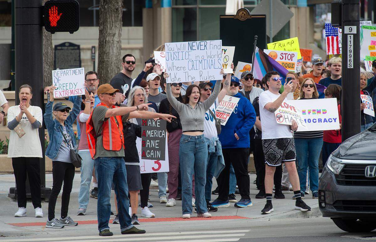 Demonstrators hold signs while they walk south along Main Street during a pro-democracy march that took aim at the Trump administration’s policies Saturday, March 29, 2025 in downtown Kansas City.