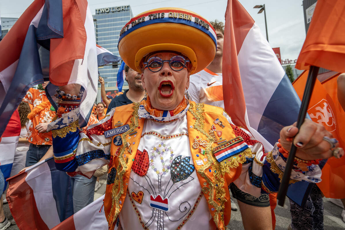 Miek van Rens-Verbers, known as the "Queen of Cheese" for her signature cheese hat, cheers while wearing an elaborate orange, red, white and blue outfit during the Orange Walk along Grand Boulevard on Thursday, June 25, 2026, in Kansas City.
