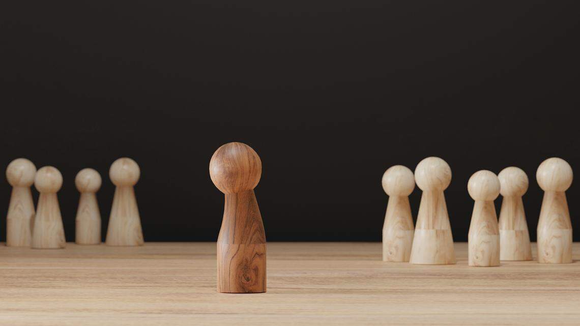 Sad wooden figure excluded from group. Concept of bullying, discrimination, isolation, loneliness, and mental health in society, workplace or school.