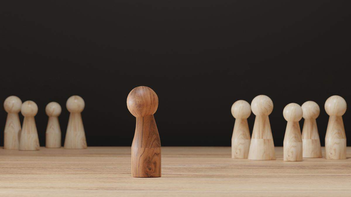 Sad wooden figure excluded from group. Concept of bullying, discrimination, isolation, loneliness, and mental health in society, workplace or school.