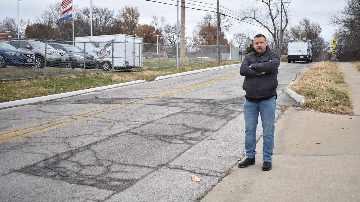 Waldo resident Frank Sereno stands beside cracked pavement at the corner of 89th Street and Wornall Rd. on Thursday, Nov. 30, 2023. Sereno was told by the city’s 311 system that all of the machines used to seal roadway cracks are out of service.