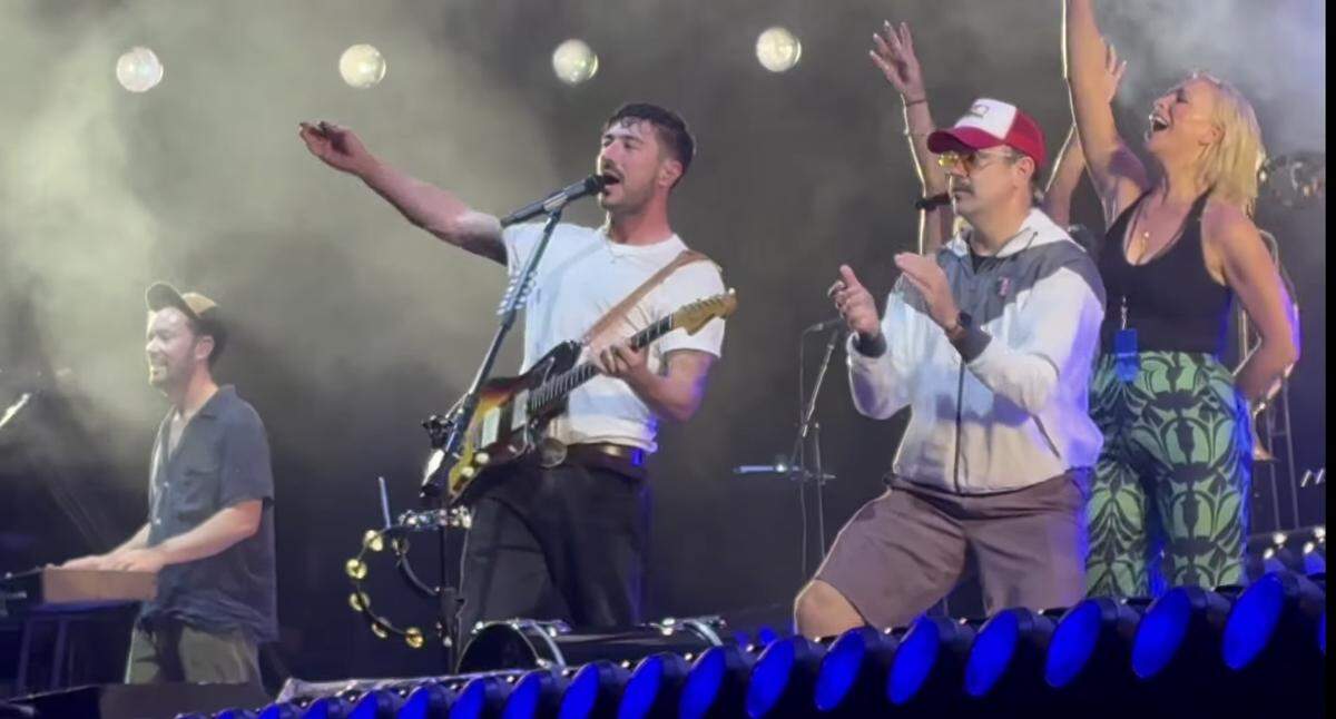 Jason Sudeikis, in the red hat, and his “Ted Lasso” castmates joined British band Mumford & Sons on stage at the Azura Amphitheater in Bonner Springs, Kan., in July 2025. The band performed the show’s theme song, which lead singer Marcus Mumford co-wrote.