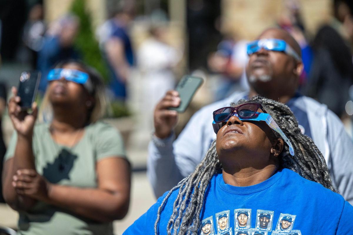Tiffany Rosada of Grandview, from left, Eugene and Bukeka Blakemore of Lenexa, watched the partial solar eclipse at Legends Outlets in Kansas City, Kansas.