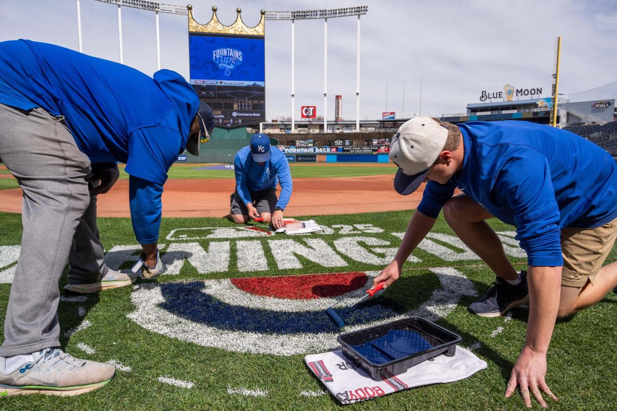 A team of Royals grounds crew workers block in red and blue paint for the MLB Opening Day logo on the field at Kauffman Stadium on Tuesday, March 25, 2025. The task is mandated by Major League Baseball for all fields to feature the logo.