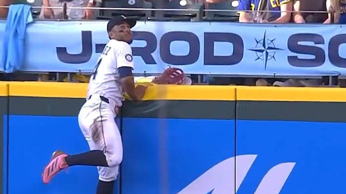 Mariners center fielder Julio Rodríguez climbed the wall trying to make a catch. Instead the ball bounced on the field in front of him.