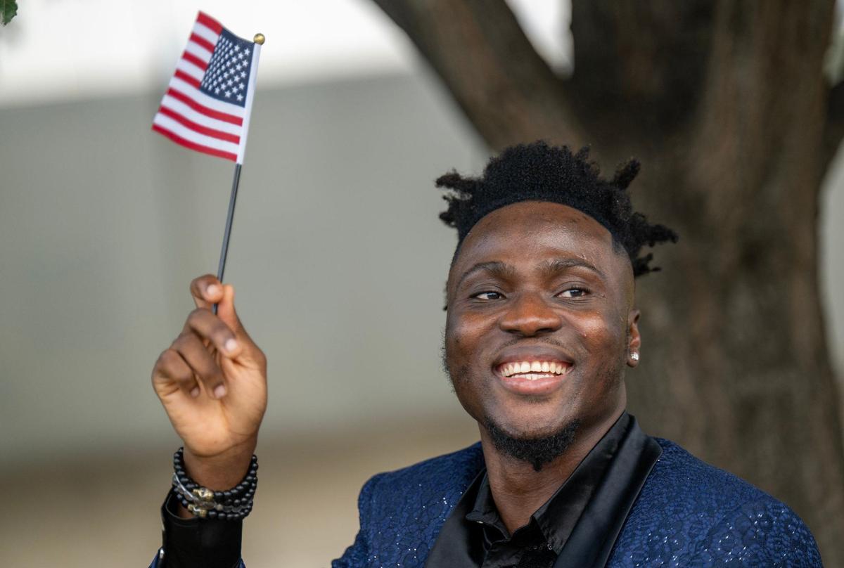 Joshua Ubogu, 29, of Jefferson City, Missouri, waves an American flag after becoming a U.S. citizen Thursday.. He plans to celebrate his citizenship with family and friends. “I’m super elated,” he said.