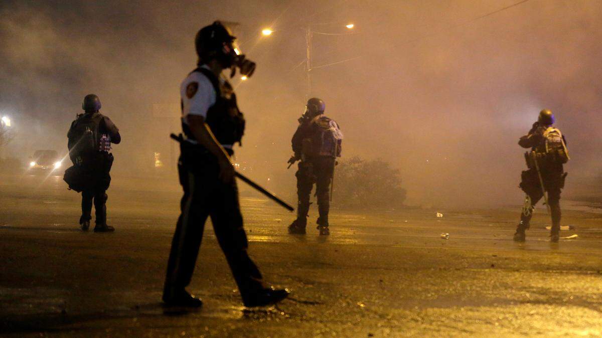In this Aug. 17, 2014 file photo, law enforcement officers watch as tear gas is fired to disperse a crowd protesting the shooting of 18-year-old Michael Brown in Ferguson, Mo.