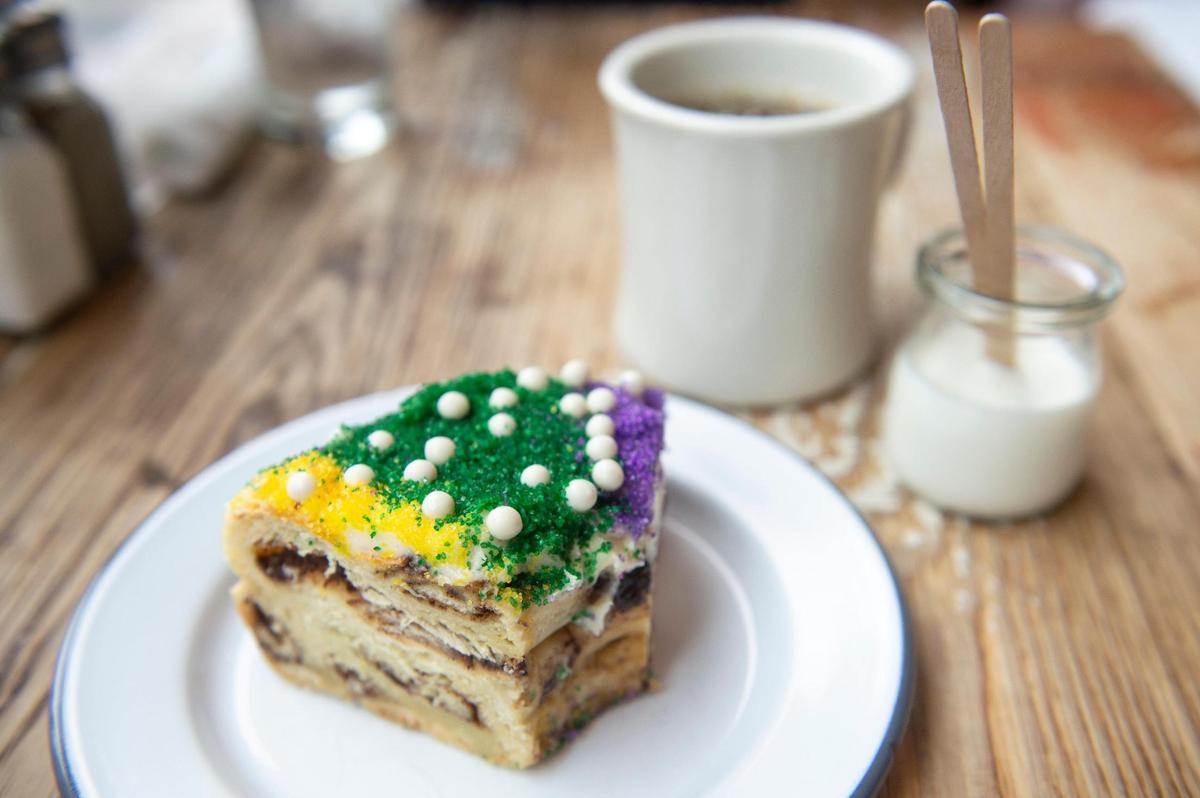 King cake is a Mardi Gras specialty that starts with a moist cinnamon roll, topped with colored cream cheese frosting and white-chocolate pearls at Willa Jean in New Orleans.