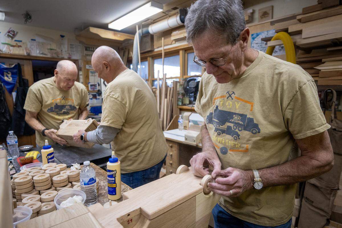 Volunteer Steve Dillon, right, of Lawrence carefully glues wheels onto a delivery-style truck at the wood shop of Jay Morris of JHM Woodworks in Lawrence, on Tuesday, Dec. 2, 2025. The trucks, 115 in all, will be donated toToys for Tots.