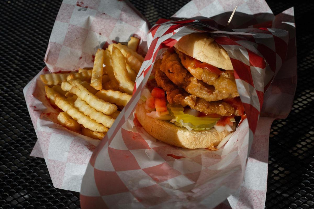 A pork tenderloin lunch sandwich, with pickles, tomato, onion and house-made sauce, is served in a basket lined with checkered paper alongside wavy fries at Kitty’s Cafe on Thursday in Kansas City.