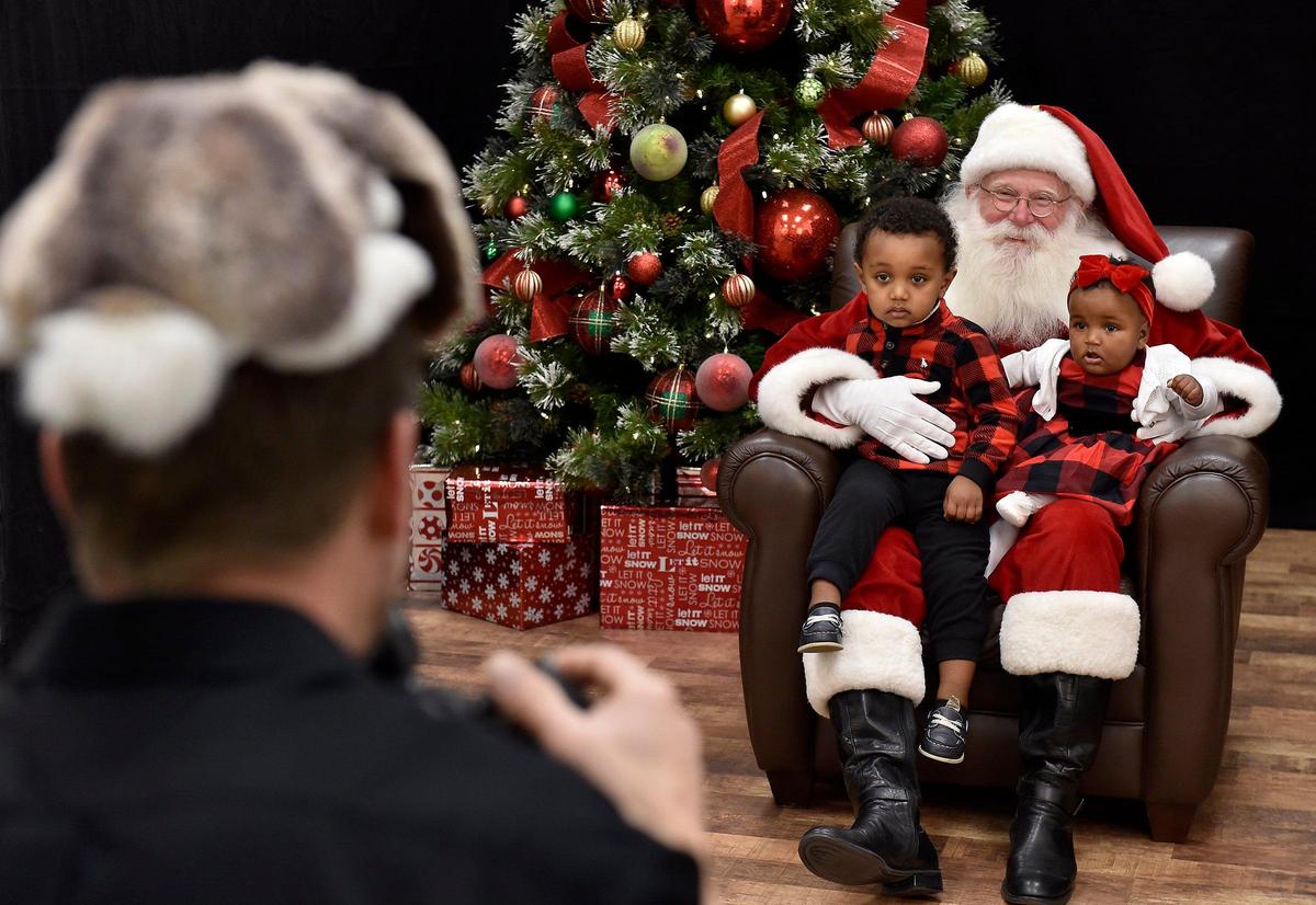 Two-year-old Peniel Wakjira of Olathe and his sister Sophia, 8 months, pose with Santa Gary as Jason Jordan tries to get them to smile.
