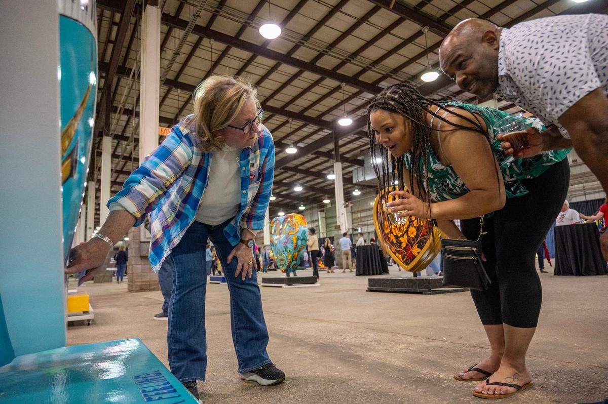 Artist Ruthie Messer Wolkey explains some Easter eggs on her heart display titled “Jazz & Blues in KC” to visitors Kelly LaGrant, left, and Brad Dacus Friday during the Parade of Hearts reveal kickoff event.
