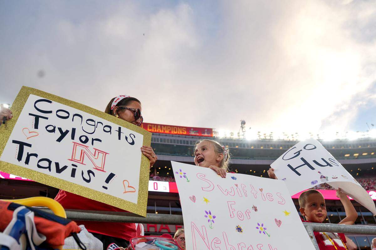 Fans hold up signs for Travis Kelce and Taylor Swift during the Kansas City Classic season opening game between the Cincinnati Bearcats and Nebraska Cornhuskers, Thursday, Aug. 28, 2025, at Arrowhead Stadium in Kansas City, Mo. The couple recently announced their engagement.