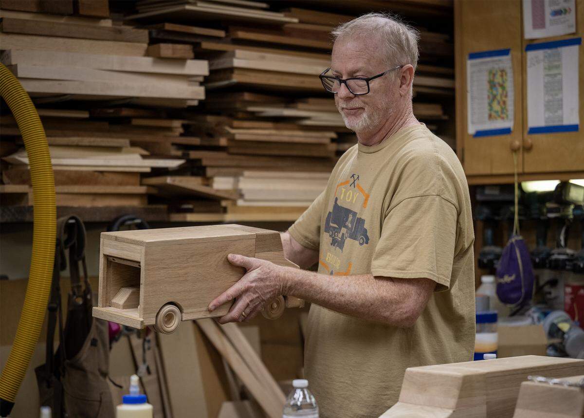 Jay Morris of JHM Woodworks carries a nearly finished wooden truck in his workshop on Tuesday, Dec. 2, 2025, in Lawrence, Kansas. Using donated wood scraps, Morris and a team of volunteers have handcrafted 115 delivery-style trucks to be distributed to children in need through the Toys for Tots program.