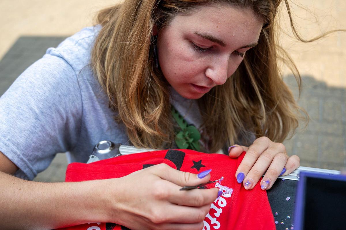 Jordan Herzberg glues charms to a T-shirt at the Customization Station by Doc Martens before Olivia Rodrigo’s Guts World Tour concert at T-Mobile Center on Friday.