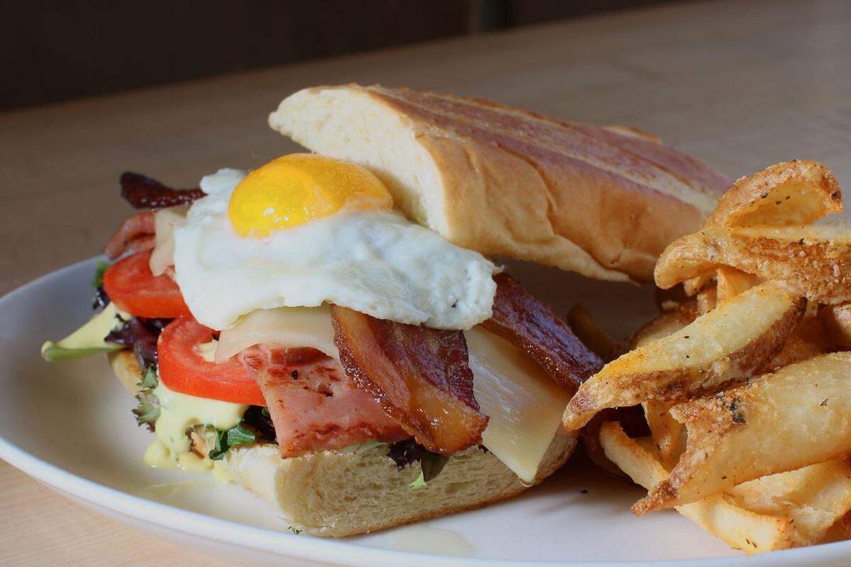 Urban Egg’s Urbano sandwich with grilled ham, applewood smoked bacon, Swiss cheese, dressed greens, tomato, black peppercorn mustard aioli and egg your way on a pressed baguette.