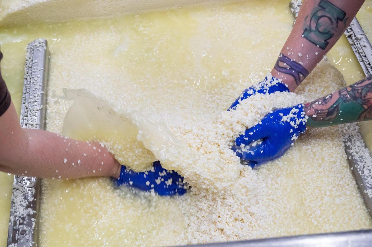 Cheesemakers move handfuls of curds to another section of a large vat that separates the curds and whey at Green Dirt on Oak.