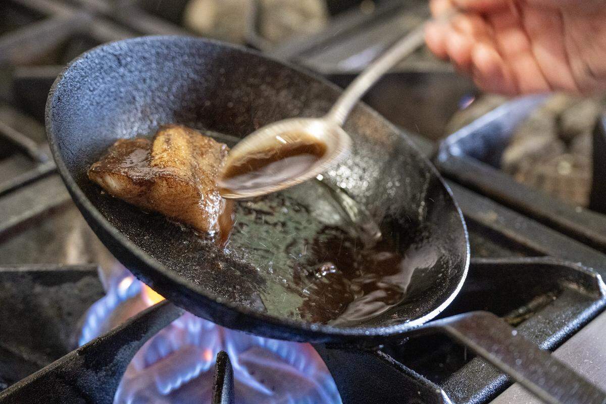 Sam Edelson, chef de cuisine, spoon-bastes Missouri catfish with house-made olive oil for Anjin's chawanmushi, finished with black olive oil, trout roe, chives, and fried heirloom corn on Monday, March 16, 2026, in Kansas City.