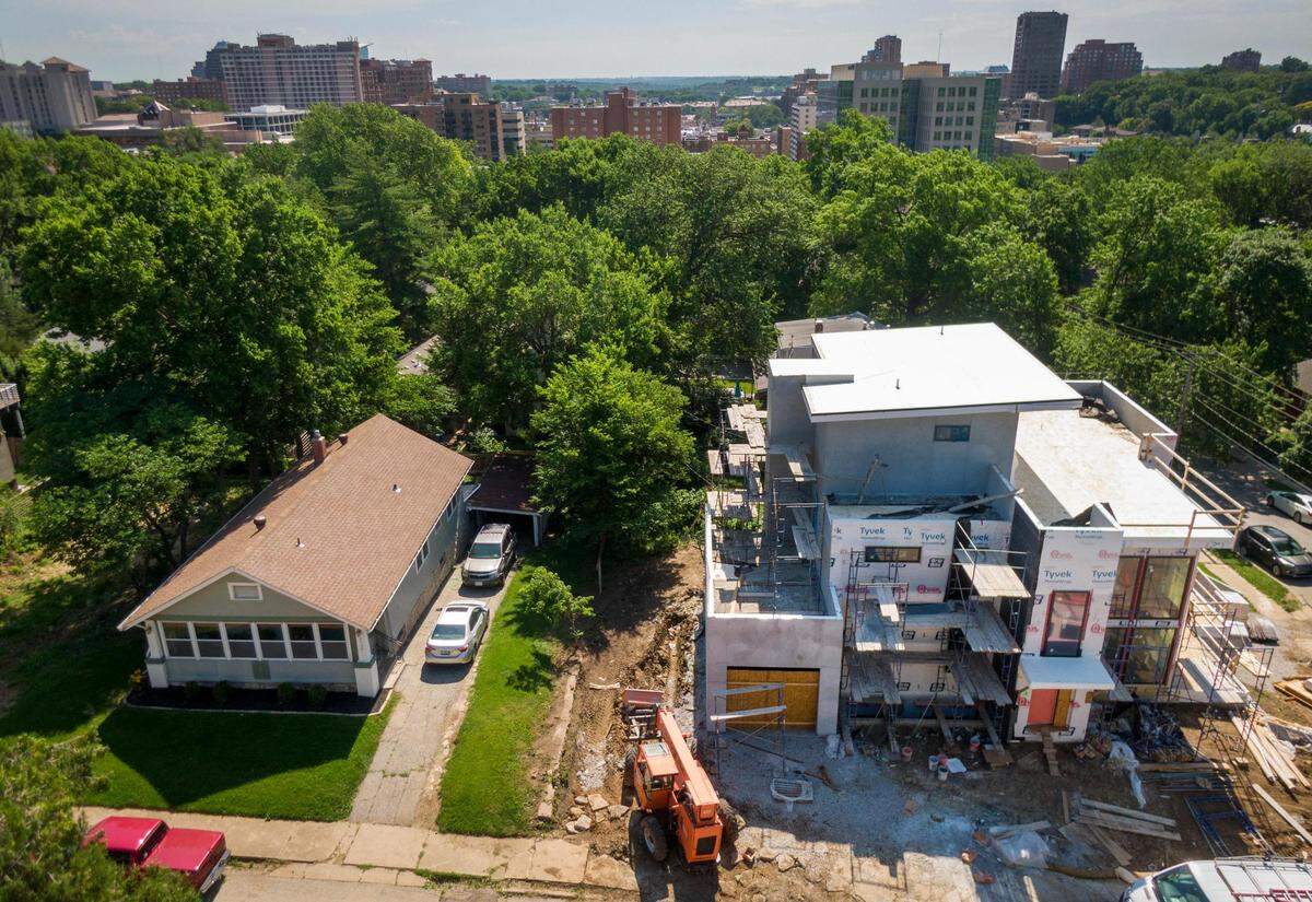 A two-bedroom, one-bath 1,024-square-foot bungalow built in 1931 is dwarfed by the new construction of a modern 5,000-square-foot home at the corner of 48th and Mercier streets in the West Plaza neighborhood of Kansas City. The new home under construction features three stories, ceiling to floor windows, seven bedrooms and a sales price of $1.7 million.