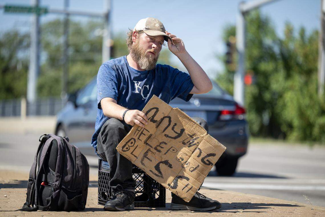 Chad Warneker, 37, of Olathe, who has been experiencing homelessness for the past nine months, sits with his sign on the median near West 87th Street and Highway 69 on Friday, Sept. 26, 2025, in Johnson County. Warneker, who works two part-time jobs, but still has no permanent housing, sometimes stays at Project 1020, a cold weather shelter in Lenexa.