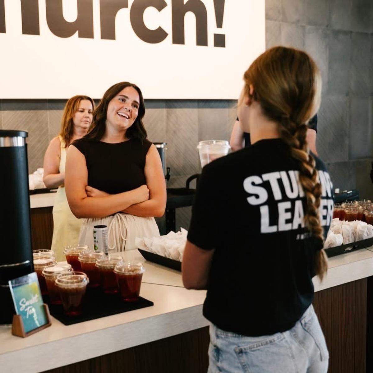A photo of Elsa McGrain volunteering with her mother Anna McGrain (behind) to serve refreshments at her church’s service in Omaha.