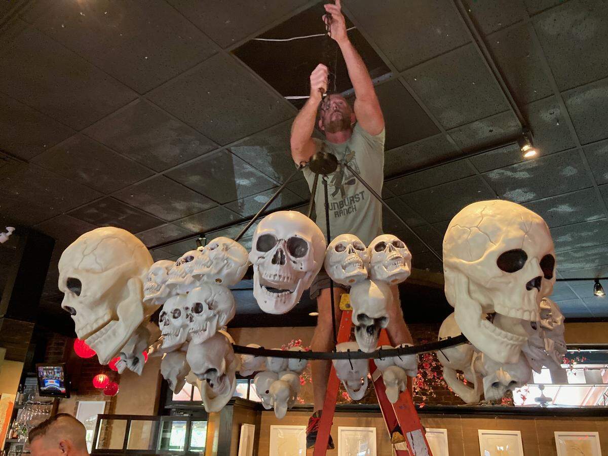 Cafe Trio co-owner Chris Youngers hangs a skull chandelier created by partner Tai Nguyen for the 2023 Halloween season. After 21 years in business, Youngers and Nguyen in September entered a partnership with W. VinZant Restaurants.