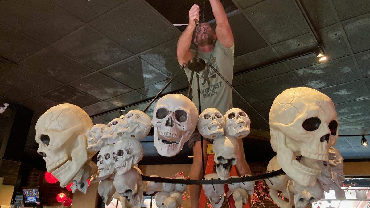 Cafe Trio co-owner Chris Youngers hangs a skull chandelier created by partner Tai Nguyen for the 2023 Halloween season. After 21 years in business, Youngers and Nguyen in September entered a partnership with W. VinZant Restaurants.