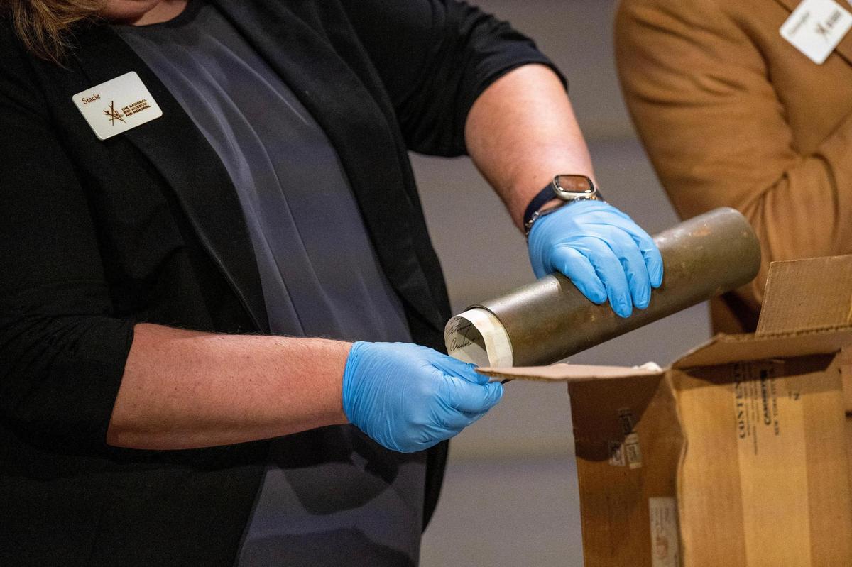 Stacie Peterson, director of exhibitions and collections at the National WWI Museum and Memorial, opens a metal cylinder containing an important historical paper during the unveiling ceremony of a 100-year-old time capsule at the museum on Wednesday, Oct. 16, 2024, in Kansas City.