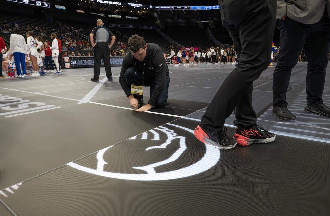 An arena crew member places white tape on the court after LED lights malfunctioned following the third quarter of a game between the Kansas Jayhawks and the UCF Knights of the Big 12 Women's Basketball Tournament at T-Mobile Center on Wednesday, March 4, 2026, in Kansas City.