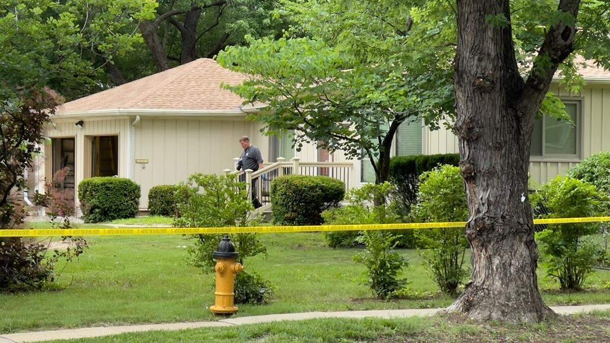 An officer walks out of a home surrounded by caution tape.